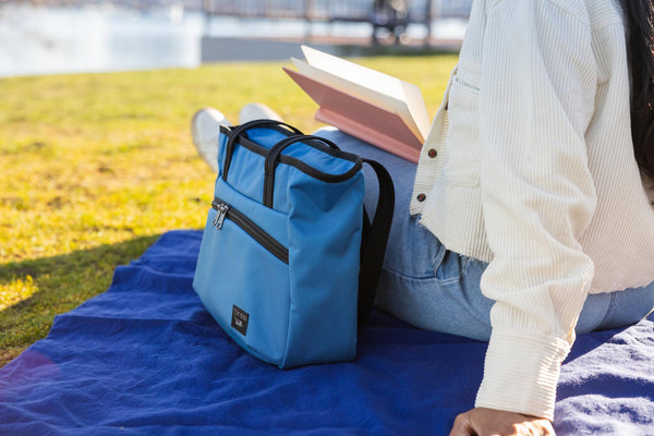 A person sitting on a blanket with a Nomad Tote at the beach.
